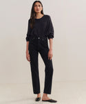 A woman with her hair down and a neutral expression stands against a plain background, wearing a loose black long-sleeve top tucked into 90s Pinch Waist Long Jeans and black slip-on shoes.