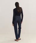 A person with long dark hair, in a black long-sleeve top, 90s Pinch Waist Long Jeans, and brown flats stands facing away from the camera against a plain light background.