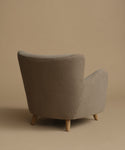 An accent chair upholstered in textured taupe fabric with light natural wood legs, set against a solid warm beige background.