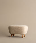The Aspen Ottoman features a compact design, cream textured fabric, and four wooden legs, displayed on a plain beige background.