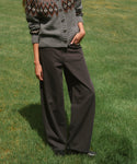 A person standing on green grass wearing dark charcoal wide-leg pants and a gray knit cardigan with a brown and cream pattern.