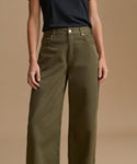 A model wearing olive green wide-leg jeans and a dark navy t-shirt, shown from the chest down against a solid beige studio background.