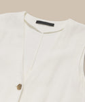 A close-up of the Callan Dress, a sleeveless white linen staple with a V-neckline and single brown button, displayed flat on a beige background with a black label inside the collar.