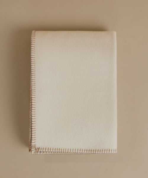 A cream-colored blanket with a stitched border, photographed flat on a matching beige background.