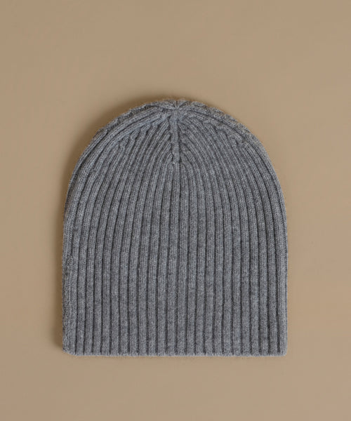 A gray ribbed knit beanie hat photographed flat against a solid beige background.