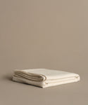The Chateau Alpaca Coverlet, neatly folded, rests on a smooth beige surface against a plain beige background, adding a touch of elegance.