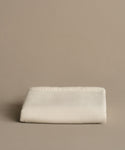 The Chateau Alpaca Coverlet, soft and neatly folded with stitched edges, rests on a plain beige surface against a matching beige background.