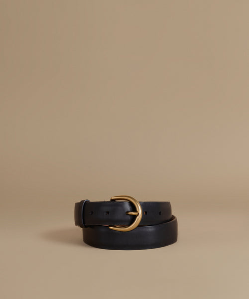 A black leather belt with a polished gold-tone metal buckle, neatly coiled on a warm beige studio background.