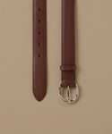 A brown leather belt shown vertically against a solid beige background, displaying both the strap end with holes and the buckle.