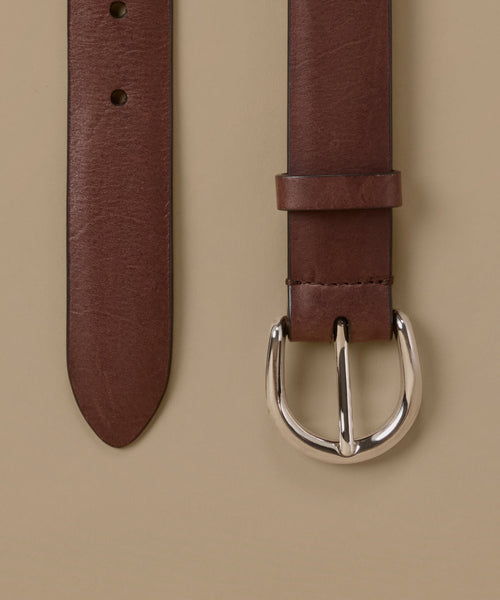 A close-up of a brown leather belt showing the strap end and buckle against a solid beige background.