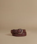 A dark brown leather belt with a silver-tone metal buckle, neatly coiled on a solid beige background.