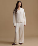 A woman modeling a matching cream knit sweater and wide-leg trousers set against a solid beige studio background.