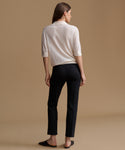 A woman shown from the back wearing a cream-colored knit polo shirt and black trousers, standing against a solid beige studio background.