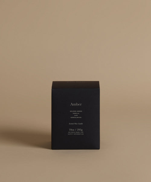 A candle box with the scent Amber across the front against a beige background.