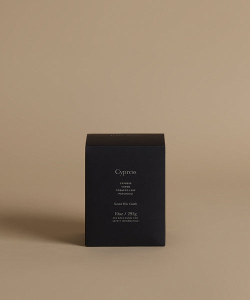 A candle box with the scent Cypress on the front against a beige background.