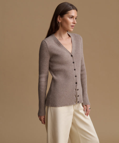 A woman wearing a ribbed knit button-front cardigan in taupe and cream wide-leg trousers, photographed against a solid warm beige studio background.