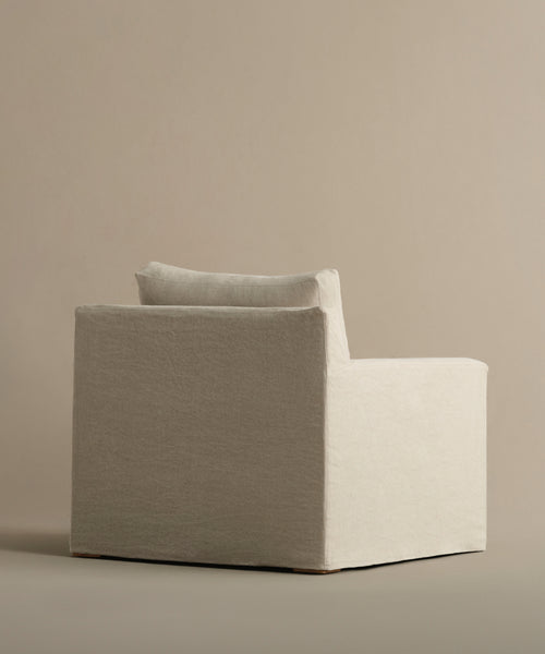 The Harbor Chair, inspired by minimalist design, features a boxy shape, wide seat, and single back cushion in light beige Drift Linen upholstery, shown against a neutral backdrop.