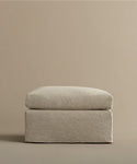 The Harbor Ottoman features a minimalist, square linen design with a cushioned top and clean lines, set against a matching beige background—a refined reflection of Jenni Kayne Furniture’s timeless style.