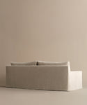 The Harbor Sofa features a modern, minimalist design with linen upholstery and two back cushions, set against a light beige background. Its clean lines and neutral color offer a calm, contemporary vibe.