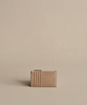 A compact Leather Card Holder in taupe with multiple card slots and a top zipper, ideal for light travel. Shown against a plain beige background.