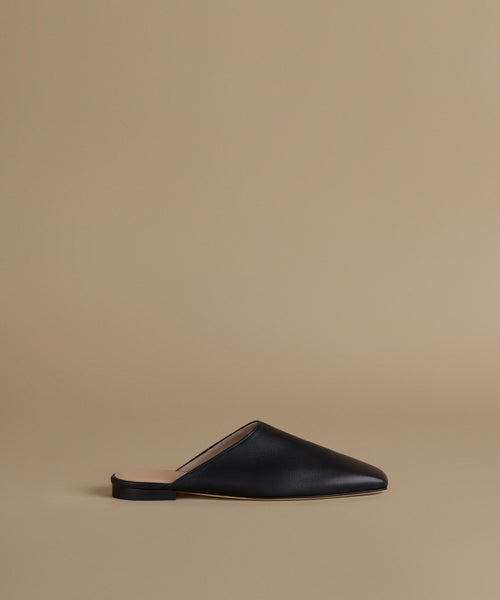 A single black leather mule slipper with a pointed toe and flat sole, shown in profile against a solid beige background.