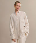 A woman with blonde hair tied back smiles softly while standing against a plain beige backdrop, wearing the oversized Linen Colby Shirt in light beige with matching pants.