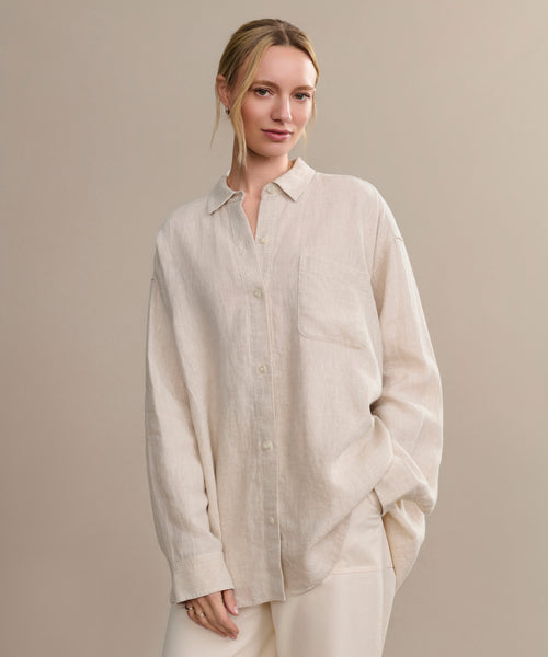 A woman with blonde hair tied back smiles softly while standing against a plain beige backdrop, wearing the oversized Linen Colby Shirt in light beige with matching pants.