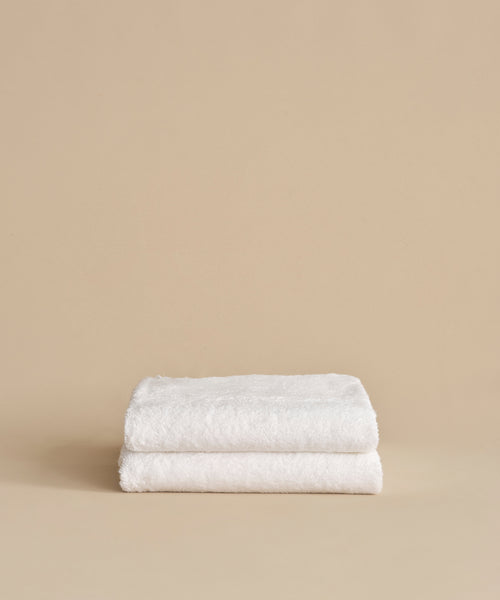 Two neatly folded Loom Bath Sheets, crafted from a luxurious cotton modal blend, are stacked on top of each other against a plain beige background.