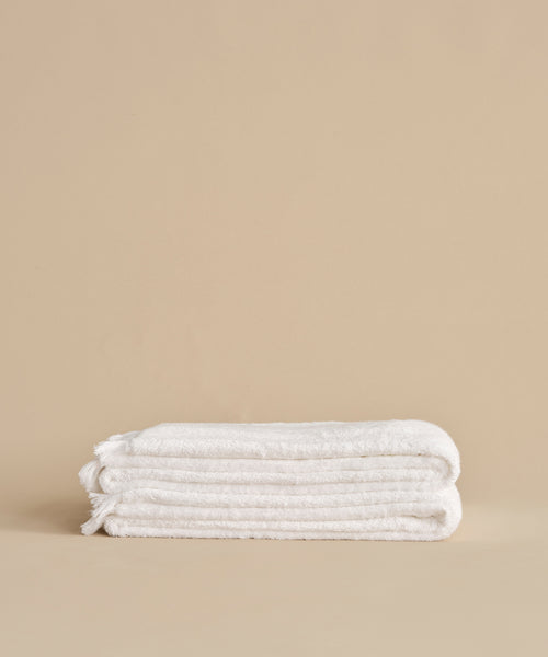 The Loom Bath Sheet, ultra-soft and white, is neatly folded on a neutral beige surface with a plain beige background.