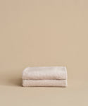 Two neatly folded, super-soft Loom Bath Sheets in beige are stacked atop each other against a plain beige background.