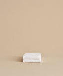 Two super-soft Loom Hand Towels, neatly folded and stacked against a plain beige background, make a perfect bathroom essential.