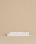 The Loom Hand Towel, ultra-soft and neatly folded in classic white, is displayed on a smooth beige surface with a coordinating beige background—an essential for any bathroom.