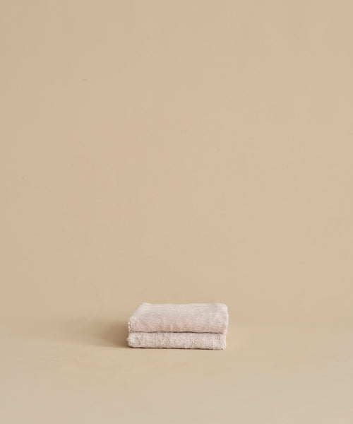 The Loom Hand Towel, made from soft cotton modal in beige, is neatly folded and placed on a matching surface and background, creating a calm and minimalistic look.