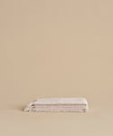 Two neatly folded Loom Hand Towels are stacked on a matching beige surface with a plain beige background, creating a serene bathroom essential display.