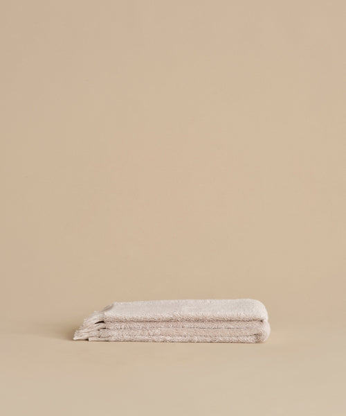 Two neatly folded Loom Hand Towels are stacked on a matching beige surface with a plain beige background, creating a serene bathroom essential display.