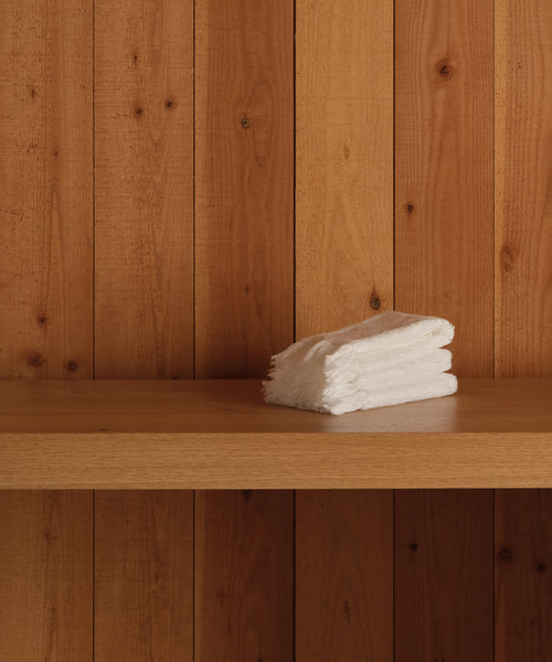 A stack of neatly folded Loom Wash Cloths, crafted from soft cotton modal, sits on a wooden shelf against vertical wooden panels—a must-have bathroom essential.