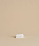 The Loom Wash Cloth, neatly folded, rests on a plain beige surface with a matching background, showcasing a minimalist and clean bathroom essential.