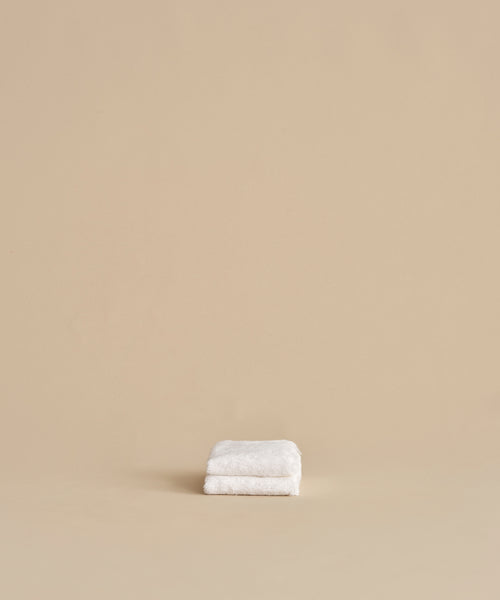 The Loom Wash Cloth, neatly folded, rests on a plain beige surface with a matching background, showcasing a minimalist and clean bathroom essential.