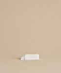 The Loom Wash Cloth, made from white cotton modal, is neatly folded on a beige surface with a plain beige background, showcasing a minimalist and clean bathroom essential.
