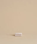 The Loom Wash Cloth, a small and super-soft beige essential, is neatly folded on a matching surface with a plain beige background—perfect for any bathroom.