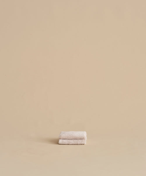 The Loom Wash Cloth, a small and super-soft beige essential, is neatly folded on a matching surface with a plain beige background—perfect for any bathroom.
