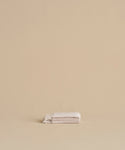 A neatly folded Loom Wash Cloth in super-soft light beige rests on a matching surface with a plain beige background, creating a minimalist and serene look—ideal as a bathroom essential.