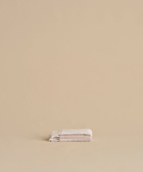 A neatly folded Loom Wash Cloth in super-soft light beige rests on a matching surface with a plain beige background, creating a minimalist and serene look—ideal as a bathroom essential.