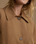 Close-up of a model wearing a tan button-up shirt with a pointed collar and dark buttons, set against a warm beige background.