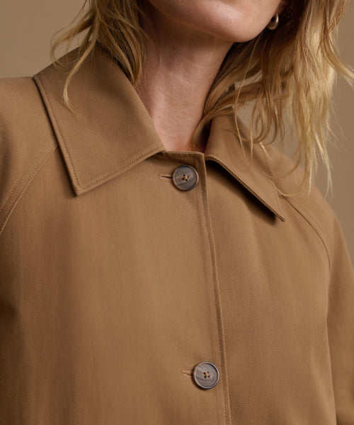 Close-up of a model wearing a tan button-up shirt with a pointed collar and dark buttons, set against a warm beige background.