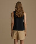 A woman shown from the back wearing a sleeveless black top and beige shorts against a plain warm taupe studio background.