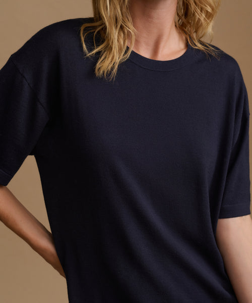 A model wearing a navy blue tee with stripe pants against a beige background.
