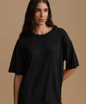 A woman modeling an oversized black short-sleeve crewneck t-shirt against a solid warm beige studio background.