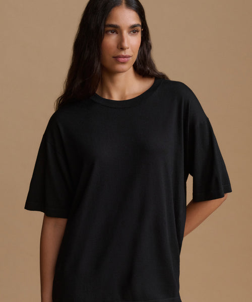 A woman modeling an oversized black short-sleeve crewneck t-shirt against a solid warm beige studio background.