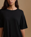 A close-up of a model wearing a black short-sleeve crewneck t-shirt against a solid warm brown background.